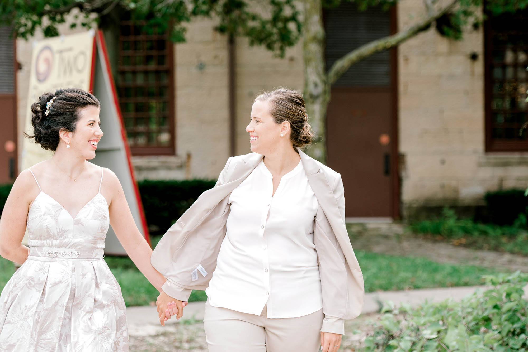 Bride in dress and Bride in suit hold hands