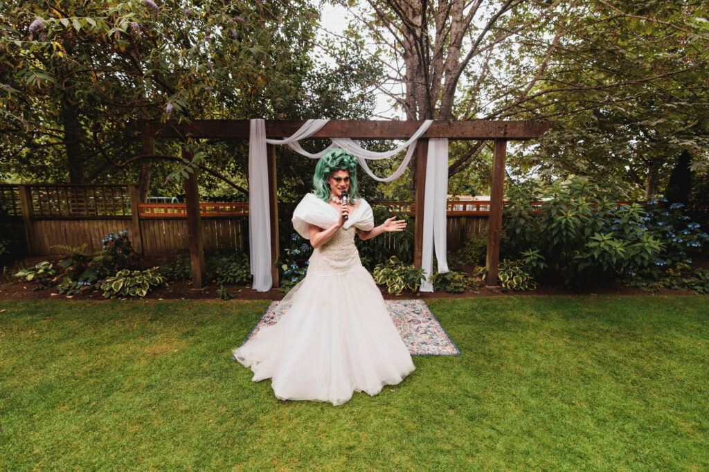 a drag queen stands on a grass lawn in a wedding dress