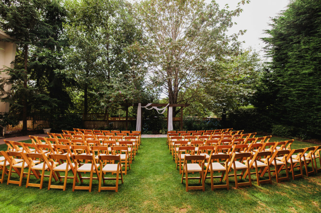 wooden chairs are set up on a grass lawn in front of a wood arbor with white fabric draping for a wedding