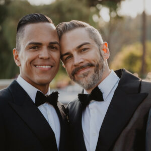 two grooms in black tuxes with feather bow ties