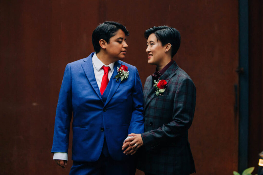 couple smiling at each other at their wedding, wearing suits