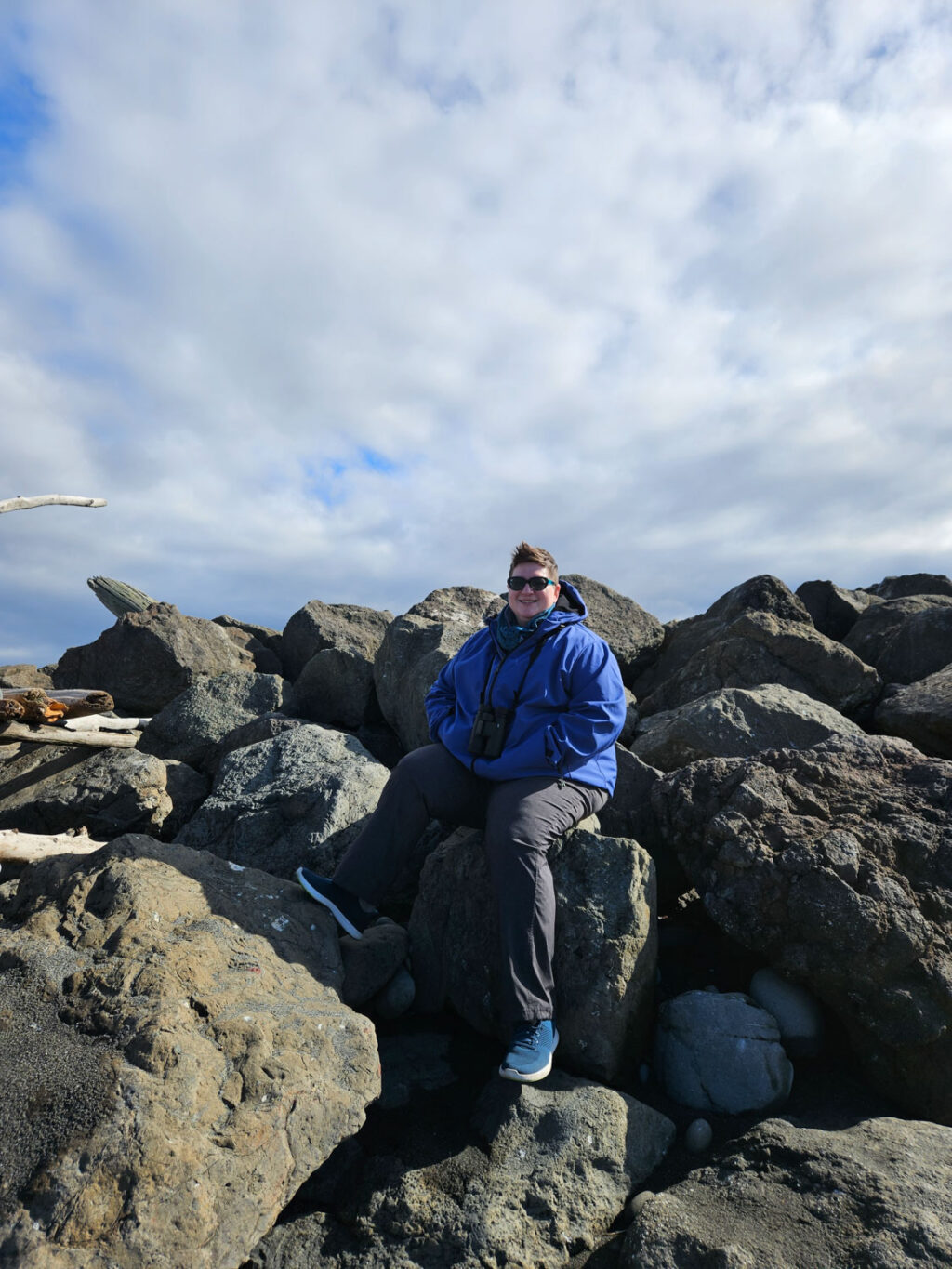 Cindy Savage, owner of Aisle Less Traveled, sitting on rocks and wearing a blue jacket