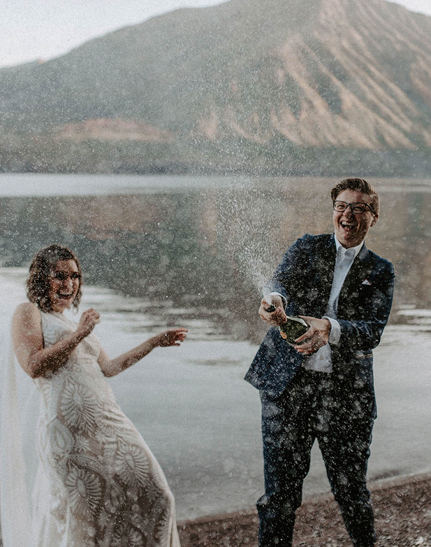 brides celebrating their wedding at a lake by popping champagne