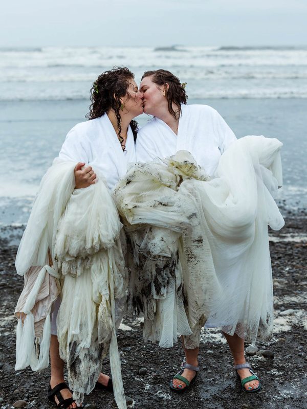 Alice and Martha, two brides standing on the beach with dirty wedding dresses after trash the dress