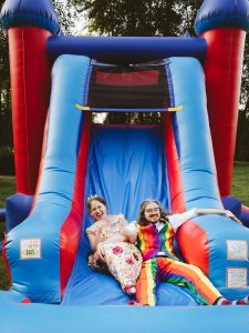 couple sliding down the slide of a bouncy house at their wedding