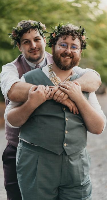 two grooms wearing flower crowns and standing together