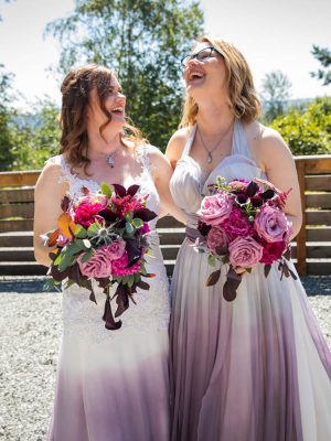 Brides wearing purple ombre wedding dresses and holding bouquets laughing together