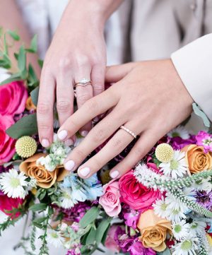 brides with rings holding hands with floral bouquets