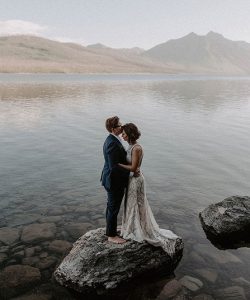 brides standing together on rock at lake elopement